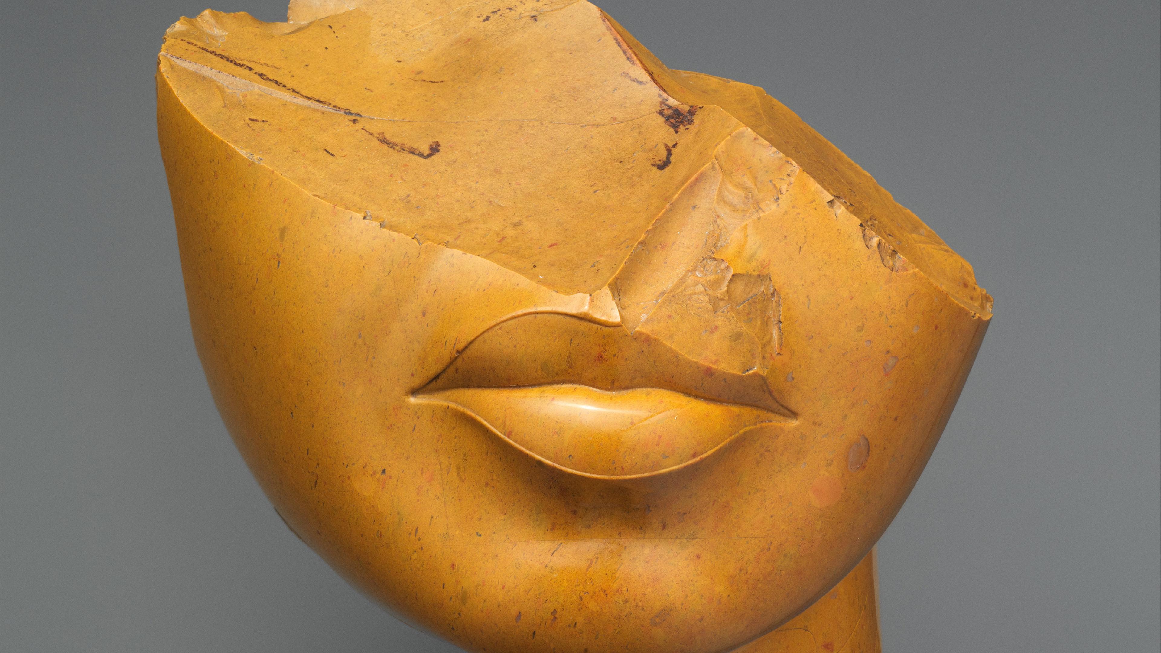 Fragment of a Queen's Face made out of yellow jasper. Only the bottom half of her face, her lips and chin are discernible.