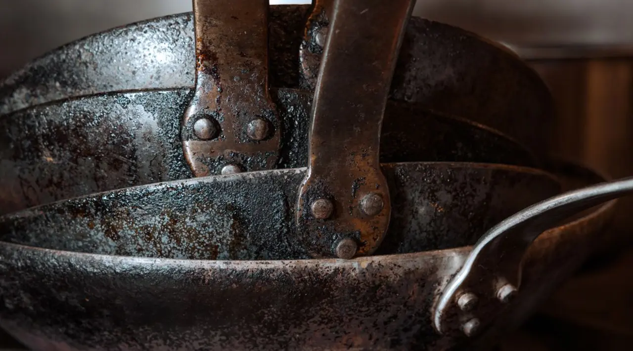 Stacked, well-used cast iron pans with visible handles and signs of wear form a rustic, culinary theme.