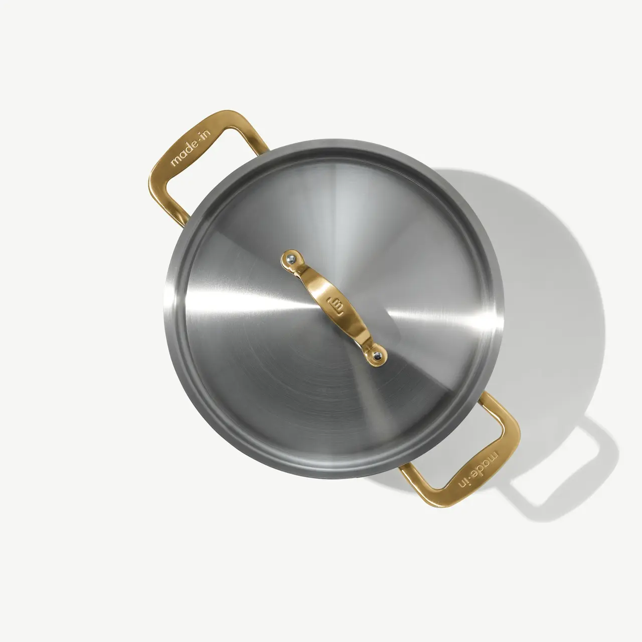 A stainless steel pot with a lid and gold-tone handles is displayed from a top-down perspective.