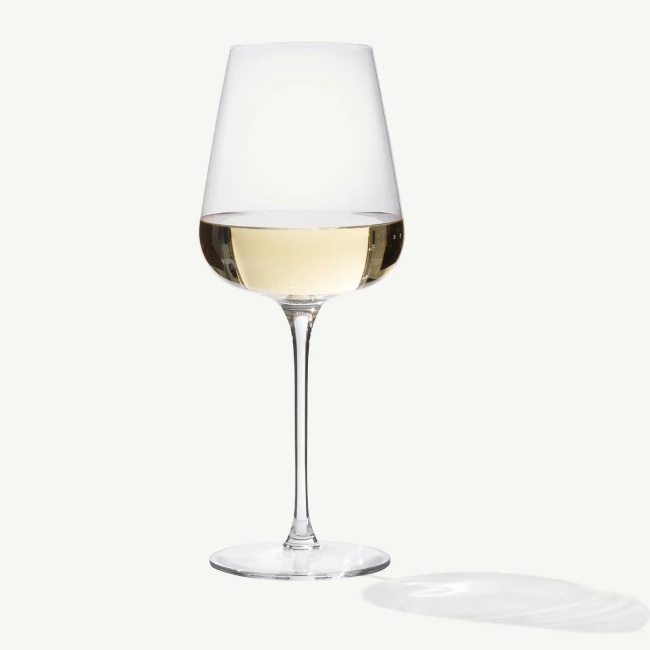 A clear wine glass filled with white wine casts a subtle shadow on a light background.