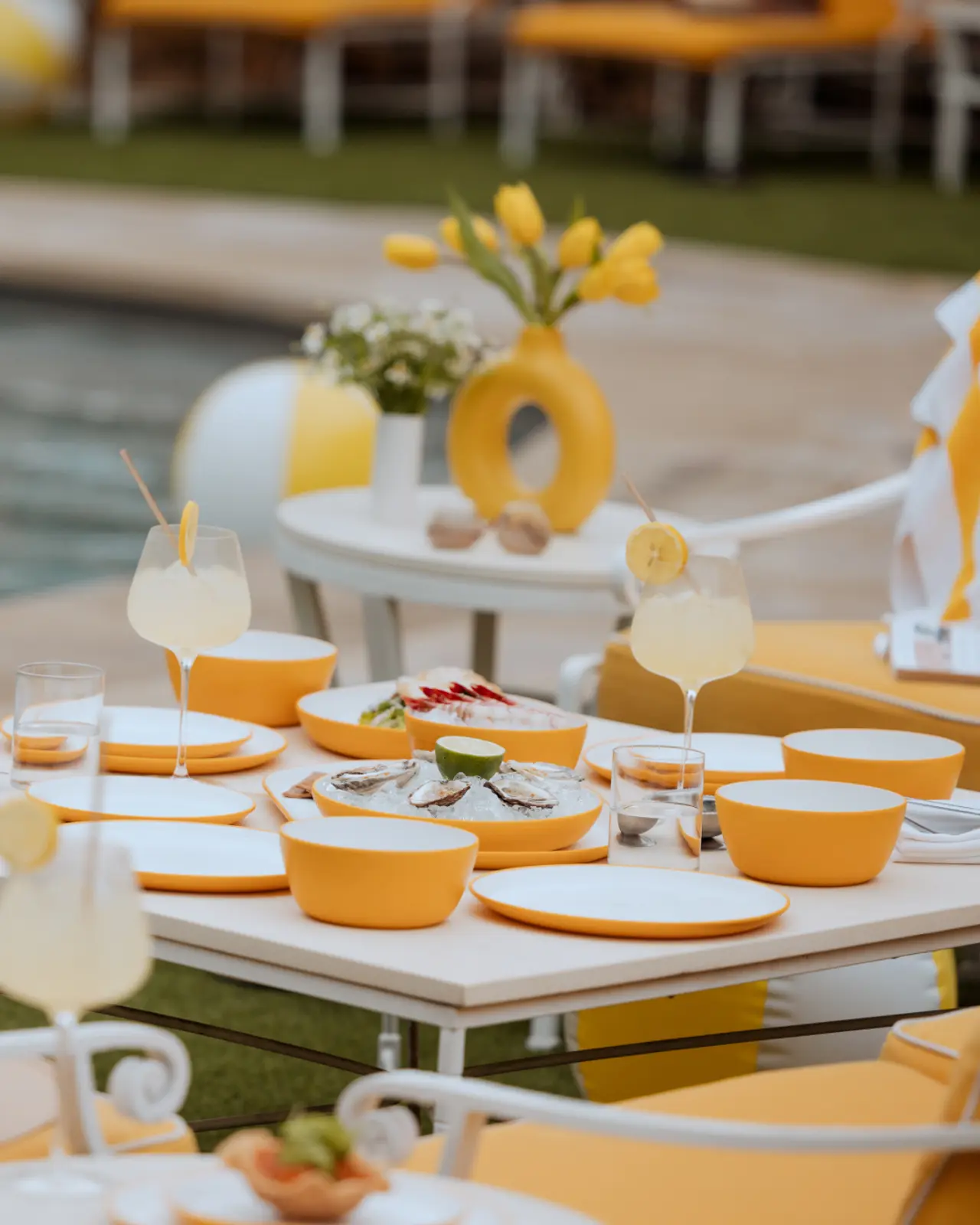 A neatly arranged outdoor dining table features a yellow color theme with matching dishes, glasses, and decorative elements.
