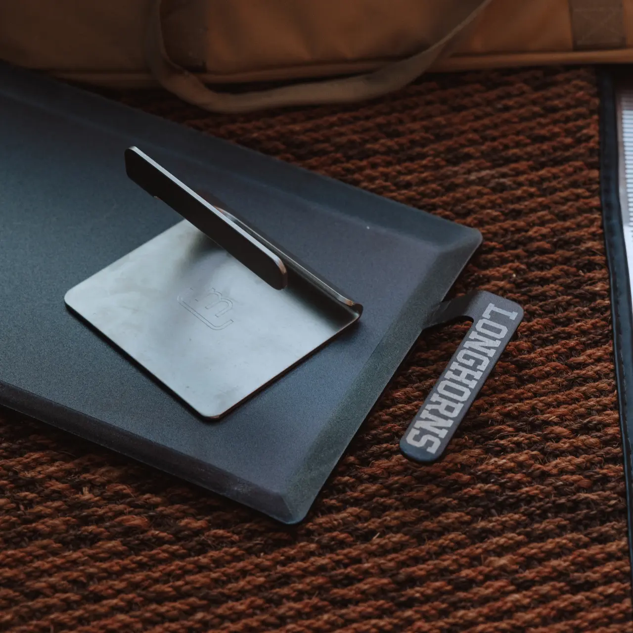 A closed laptop lies on a textured surface with a smartphone propped atop it and a luggage tag reading "Stratocruiser" nearby.