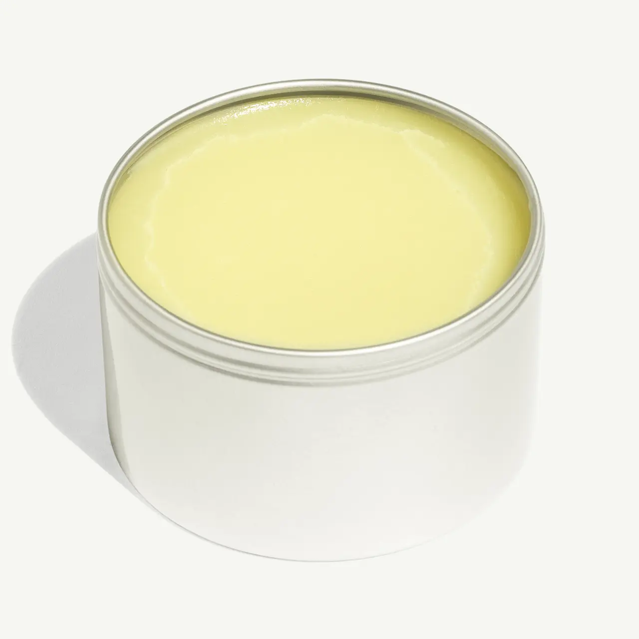 A tin filled with solid yellow balm sits against a white background.