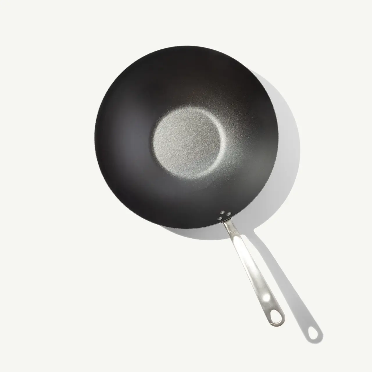 A black, round wok with a stainless steel handle sits against a light background.