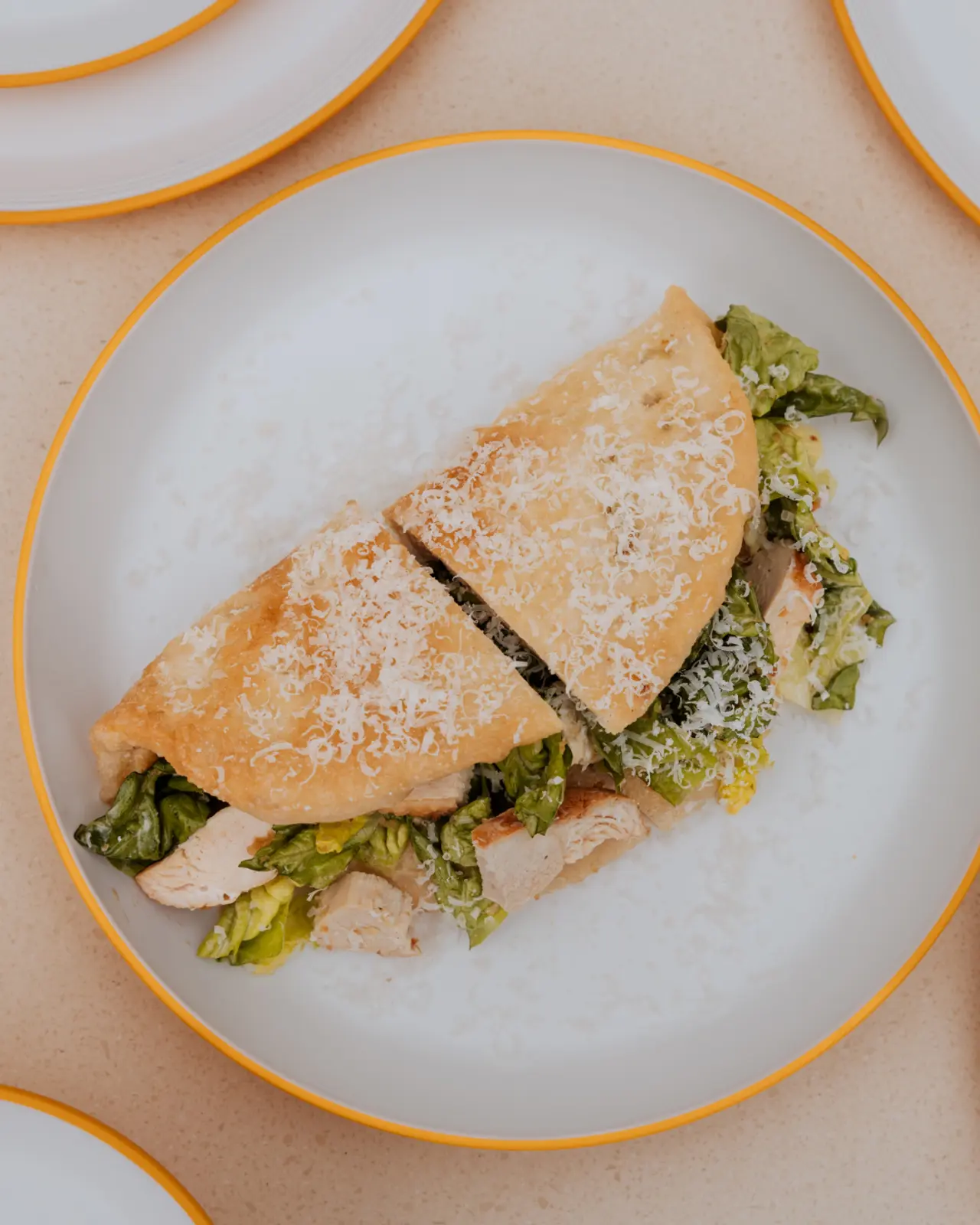 A folded sandwich with a side of greens served on a white plate with an orange rim.