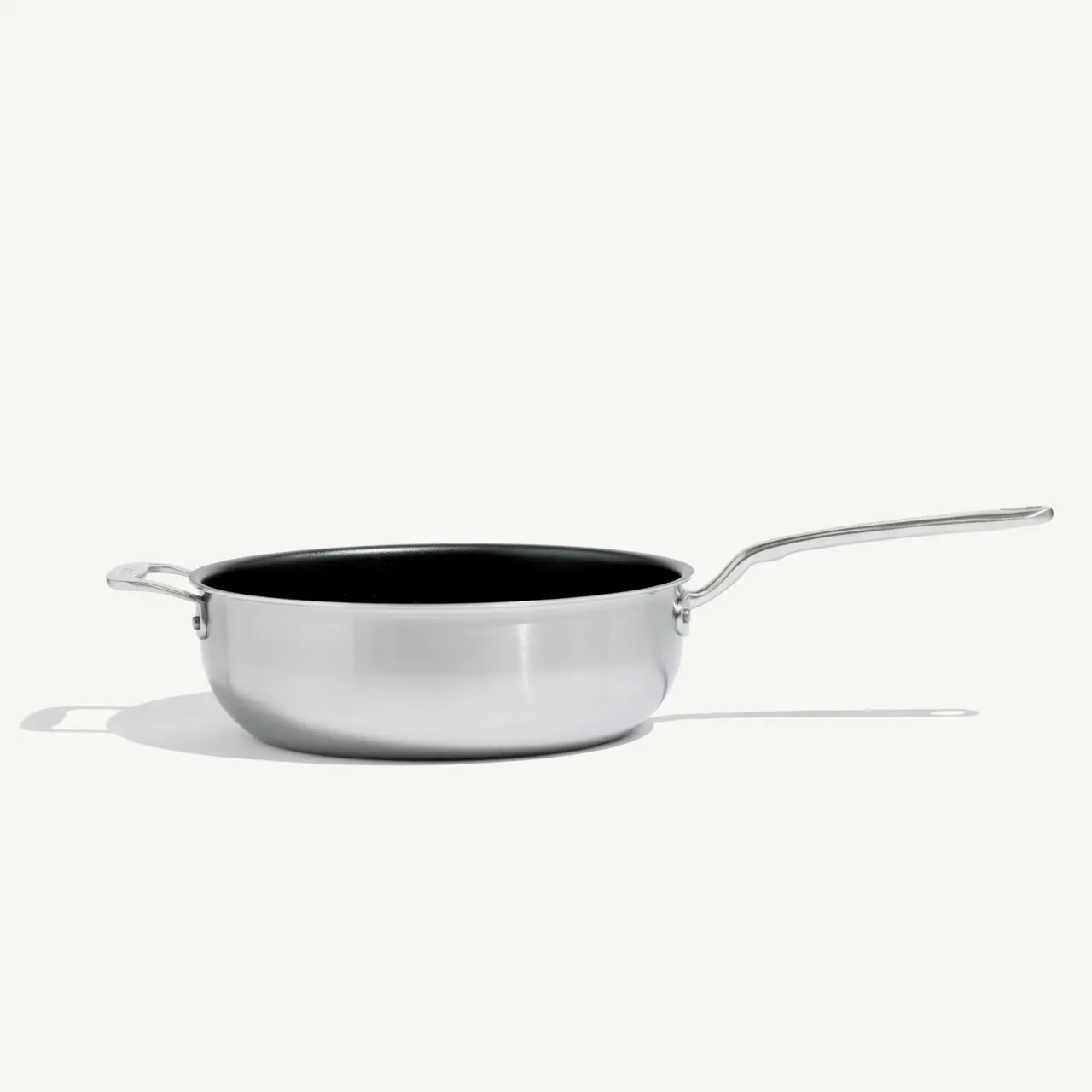 A stainless steel frying pan with a long handle casts a shadow on a light background.