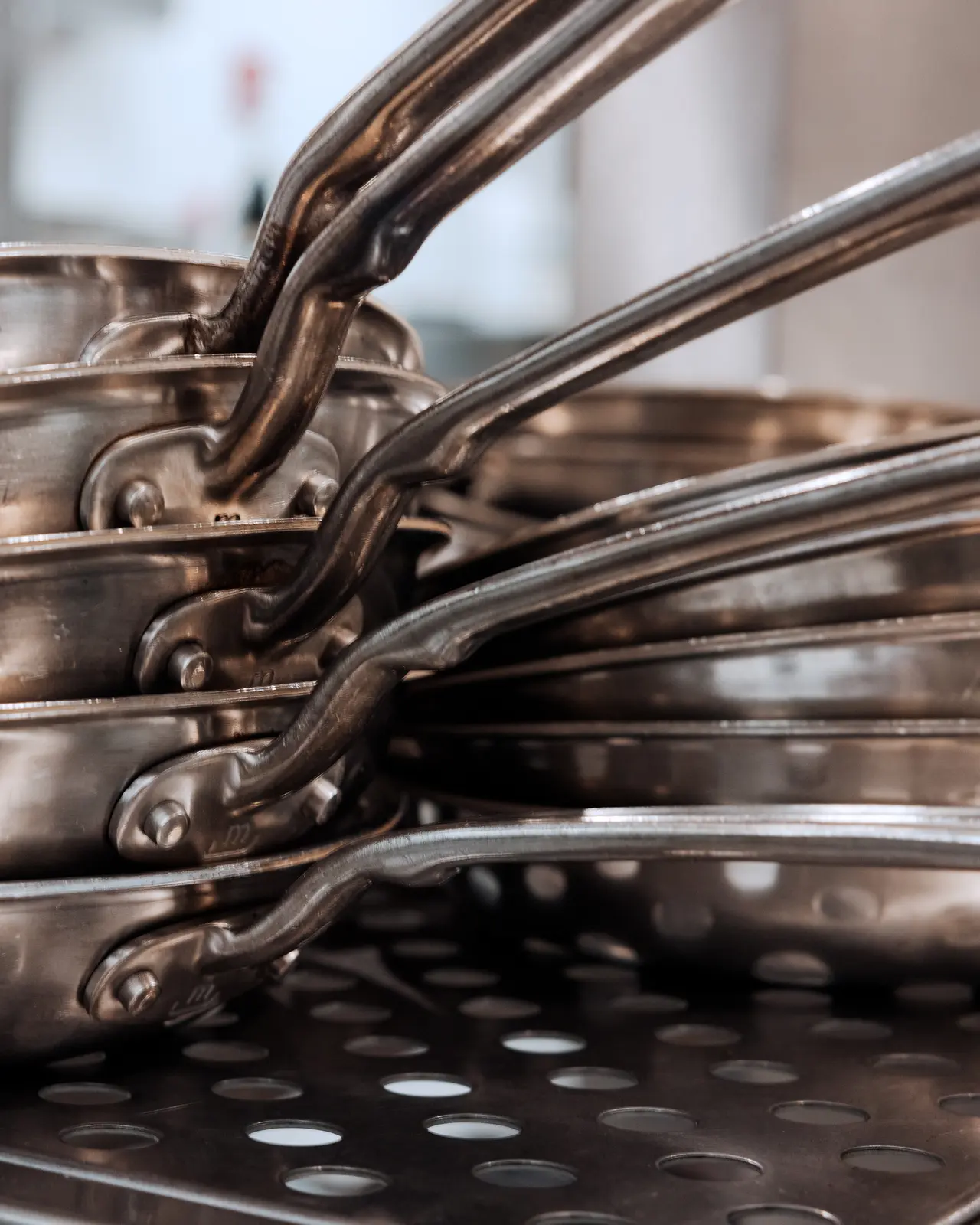 Stacked stainless steel pots with handles aligned together on a perforated surface.