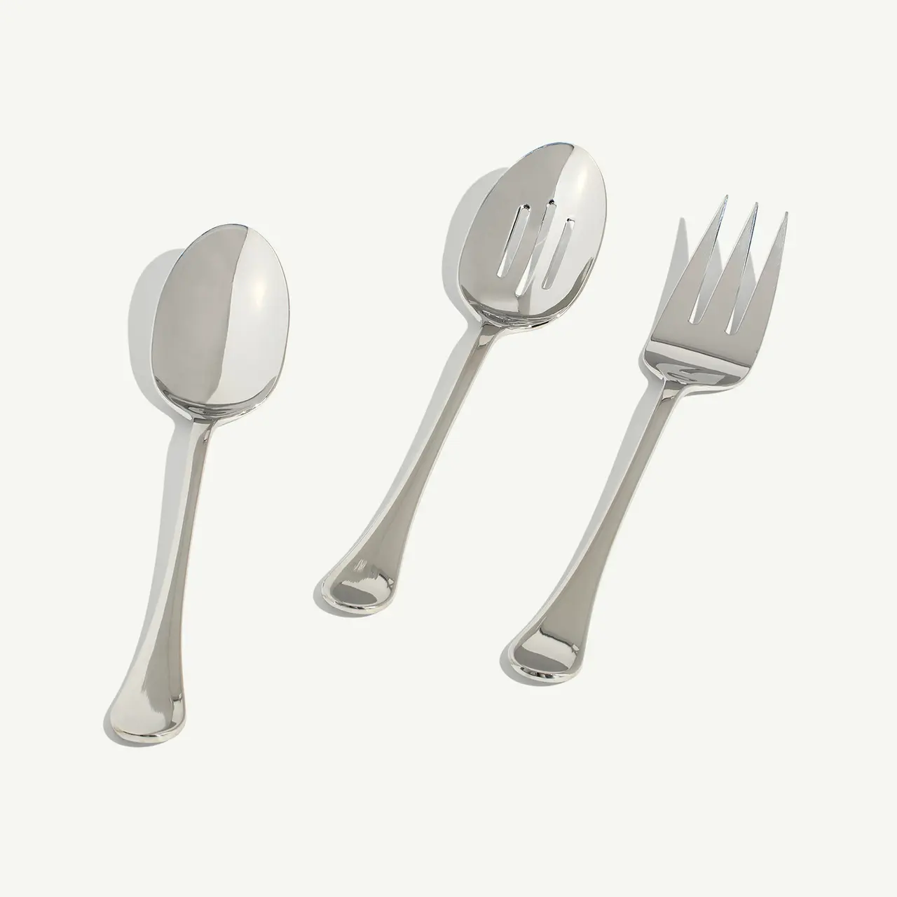 Three silver serving utensils, consisting of a spoon, a slotted spoon, and a serving fork, are arranged side by side.