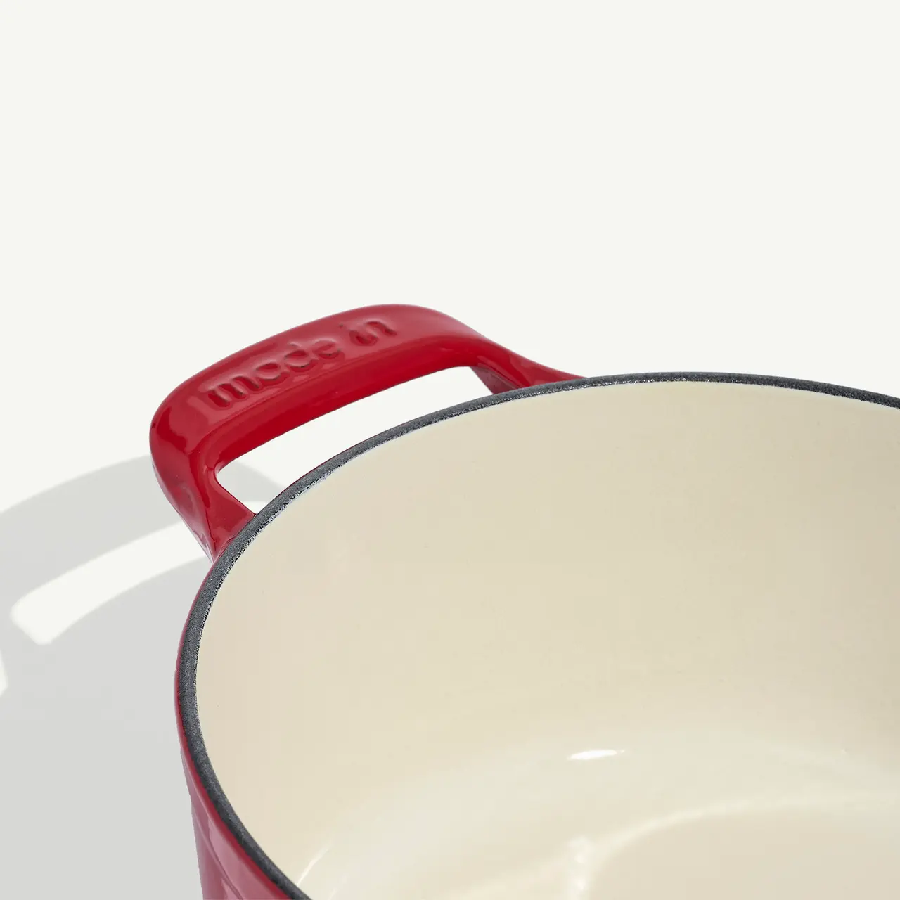 A red cast iron Dutch oven with a white interior and "made in" embossed on the handle is shown.
